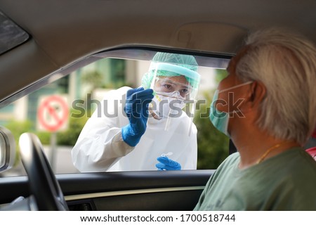 Doctor or nurse wearing PPE, N95 mask, face shield  and personal protective gown standing beside the car/road screening for Covid-19 virus, Nasal swab Test   Royalty-Free Stock Photo #1700518744