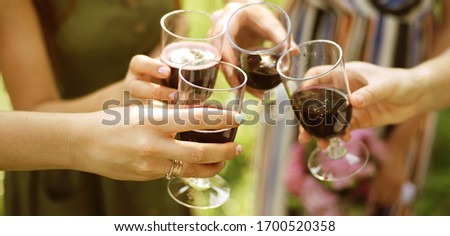 Celebration. People holding glasses of red wine making a toast outdoor on green background. Banner for website
