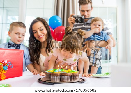 Family watching girl blowing out candles on birthday cake at home