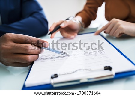 Two Businesspeople Hand Analyzing Document Over Glass Desk
