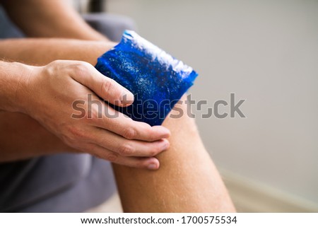 Midsection Of Man Holding Cool Gel Pack On Knee For Pain Relief Over White Background Royalty-Free Stock Photo #1700575534