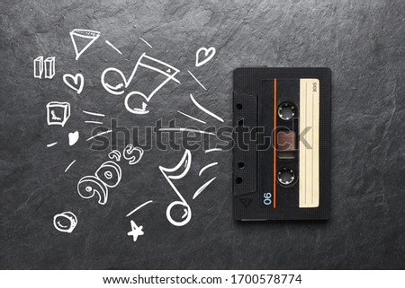 Black audio tape compact cassette and hand drawn sketch of music doodles on black background