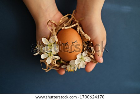 Easter egg with a face in the hands of a child decorated with blooming flowers on a blue background top view