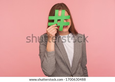 Hash sign. Portrait of woman in business suit looking through paper hashtag symbol, having fun, promoting web content and viral internet ideas, blog marketing. studio shot isolated on pink background