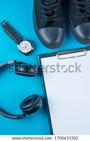 The diet plan. White sheet on the tablet among the black sneakers, headphones and clock on a bright blue background. Slimming and detox concept.