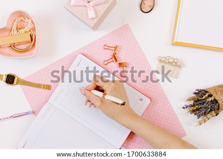 Girl keeps a diary and planning a day on stylish workplace. Female hand write in pink notebook. Women blog concept with pink notebook and golden watch. Flat lay style. 