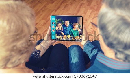 Senior couple video chatting on digital tablet with son and grandchildren due to home isolation quarantine – grandparents connecting with family on video call – old people having fun using technology Royalty-Free Stock Photo #1700671549