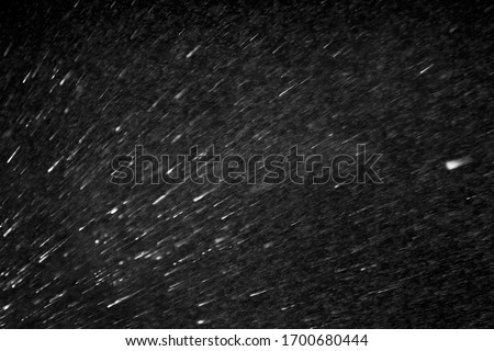 Flying white spatter spray or blizzard snow storm on black background, texture, overlay Royalty-Free Stock Photo #1700680444