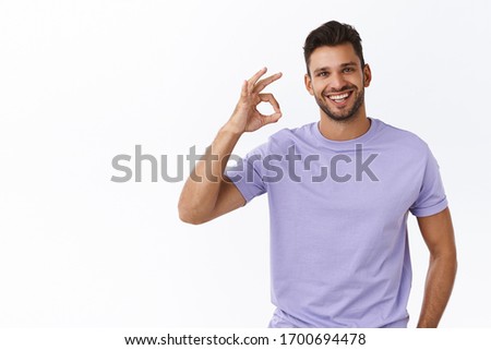 Handsome masculine smiling, encouraged man with bristle, wear purple t-shirt, showing okay, good or excellent gesture, make ok sign and grin with approval, give positive feedback, white background