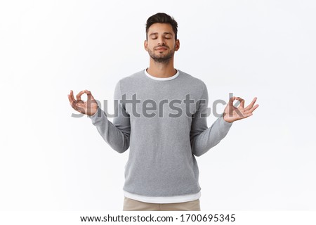 Mindful patient and relaxed young happy man, practice breathing exercises, hold hands sideways and smiling relieved, release stress during work time take break to meditate, white background Royalty-Free Stock Photo #1700695345