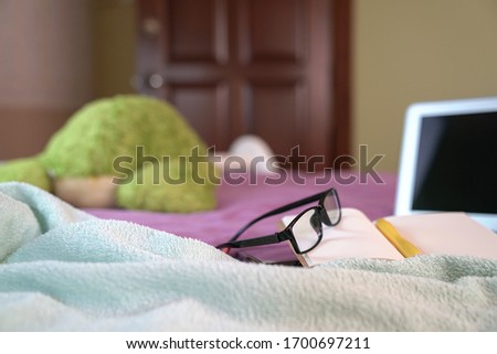 Spectacles on top of notepad and computer laptop, on top of bed.