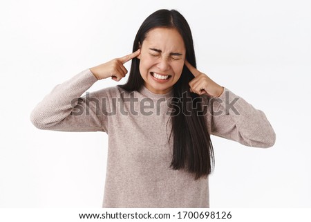 Turn-off this annoying music. Disturbed and bothered young asian college girl cant study prepare exams cause noise neighbours throw-up party, close ears with fingers, grimacing distressed
