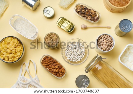 Creative flatlay with pantry staples. Glass jars with pasta, beans and chickpeas, canned goods, nuts and dried mushrooms in reusable containers. Top view pattern with  products on yellow background Royalty-Free Stock Photo #1700748637