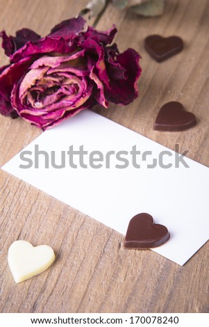 the dried rose, blank business card and chocolate hearts on a wooden table - valentines composition