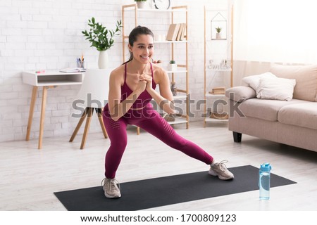 Stay home workout. Happy millennial girl doing lunges on yoga mat in light room Royalty-Free Stock Photo #1700809123