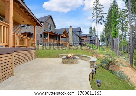 Beautiful wooden back porch with chairs on the hill and large backyard patio with fire pit and pine trees.