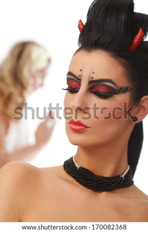 Closeup portrait of woman with professional black makeup looking like black bogy, angel at background.