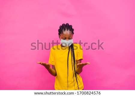 portrait picture of a beautiful african girl wearing a medical face looking her hands.