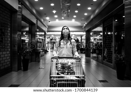 Worried woman with mask groceries shopping in supermarket,pushing trolley.Food panic buying and hoarding.Covid-19 quarantine shopper.Financial problems anxiety.Unemployed person in money crisis