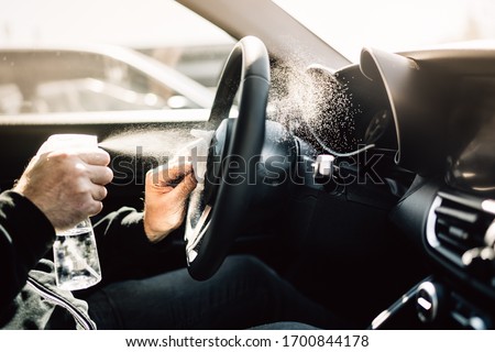 Car owner disinfecting vehicle with alcohol based sanitizing solution spray.Touched surfaces sanitation.Coronavirus COVID-19 spread prevention.Cross-contamination.Steering wheel disinfection Royalty-Free Stock Photo #1700844178