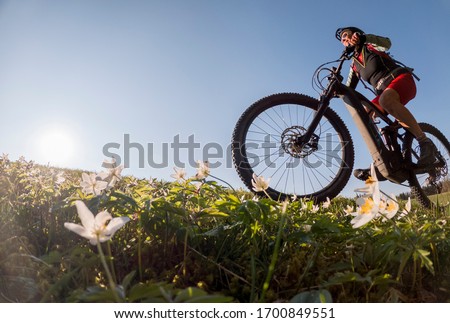 pretty senior woman riding her electric mountain bike in early springtime in the Allgau mountains near Oberstaufen, in warm evening light with blooming spring flowers in the Foreground Royalty-Free Stock Photo #1700849551