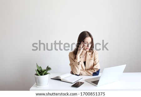 Young pretty girl sitting at her workplace in office, looking at laptop screen with angry expression. Tired and angry. 