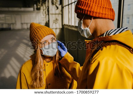 Couple in medical protective masks and gloves, dressed in yellow coats looking at each other with sadness because of coronavirus. Health care concept. Covid-19.