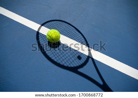 The shadow of the tennis racket and the tennis ball inside it. All on a blue tennis court. Royalty-Free Stock Photo #1700868772