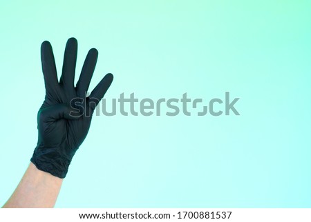 hand in sterile black gloves on a turquoise background shows different signs and symbols with fingers