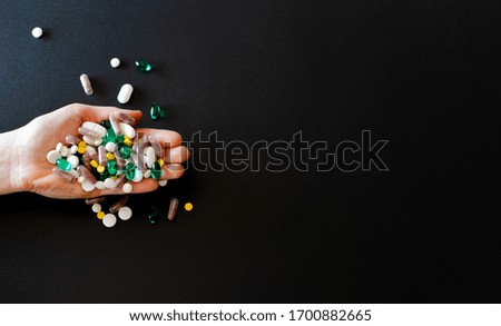 Lots of different medicine drugs, pills, tablets, capsules in woman hand on black matte background. macro photo with selective focus. Medical pharmacy background. Copy space. Horizontal frame

