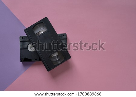 Tow VHS video tapes overlays on a pink and purple background. Minimalistic retro concept
