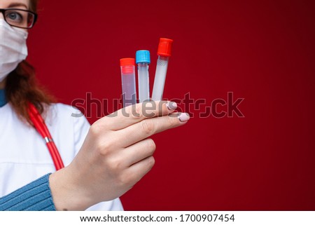 Portrait of female doctor in medical clothes with phonendoscope around her neck holds several test tubes, picture isolated on red background