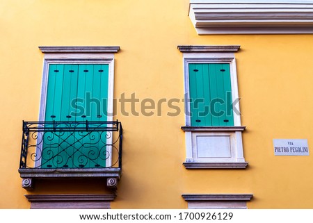 Balcony and green window on the yellow wall of a recently renovated house in the historic center of the city. Sign indicating the street named after Palladio.