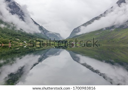 A mystical fjord with dark clouds in Norway with mountains and fog hanging over the water in a beautiful monochrome blue color. selective focus Royalty-Free Stock Photo #1700983816