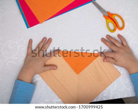 instructions step by step. a child in training at home during quarantine makes origami out of paper. children's creativity. hands close up