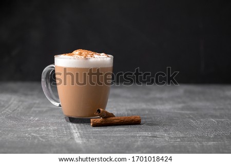 Side view of delicious cappuccino coffee with milk foam sprinkled with cinnamon in a transparent glass mug on a gray background, horizontal format
