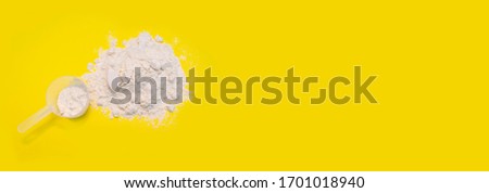 Pile of banana protein powder and measuring cup isolated on yellow background Royalty-Free Stock Photo #1701018940
