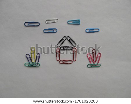 A house, flowers and the sky made with colored paper clips. Office tools for games with children.