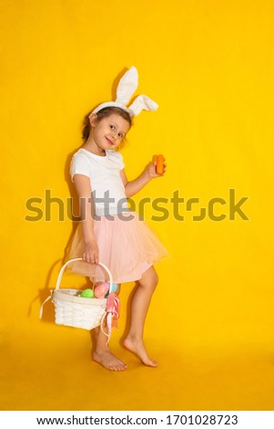 cute girl in a white t-shirt and tulle skirt on a yellow background with Bunny ears. A bright girl is holding a basket with eggs on a yellow background. pre-holiday fuss. Bright Easter.
