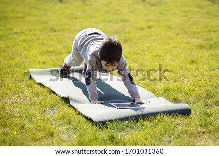 child 5 years old does sports exercises on mat. looking at tablet. lifestyle. blog concept, applications, children’s yoga, health, parenting, childhood with gadgets. development, screens. roll grass