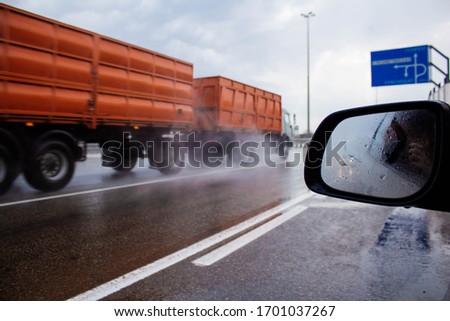 A long wet road with an orange truck. View of the road in the rain from the car window. Water splashes from under the wheels of cars. Grey, gloomy sky and noisy road.