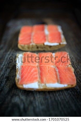 Two whole grain bread toasts with cream cheese and lightly salted salmon on a dark wooden board. Flat lay. Copy space. Concept, healthy breakfast, food, snack.