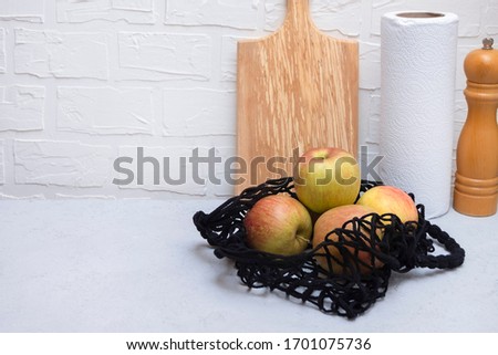 Mesh bag with apples on neutral kitchen table with copy space. Plastic waste reduce concept