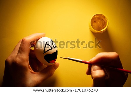 Painted white egg on a yellow background. The grimace of fear is depicted on the egg.