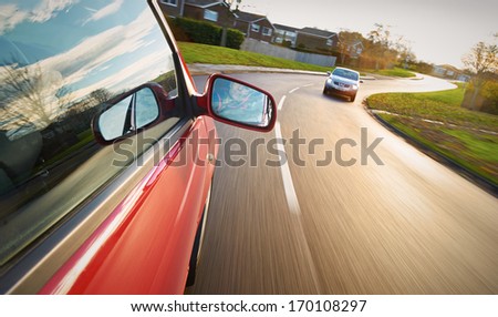 A man driving a red car towards a bend in the road. Royalty-Free Stock Photo #170108297