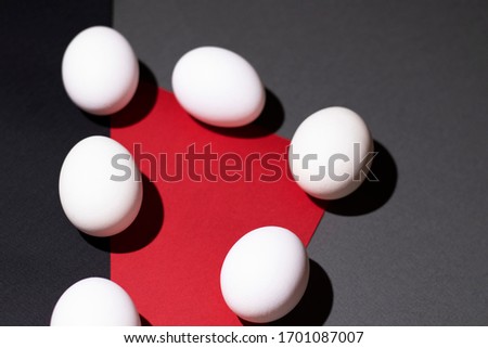 White eggs are located on a geometric background of three colors: red, gray and black. There is a place for text. Custom photo format for your design.