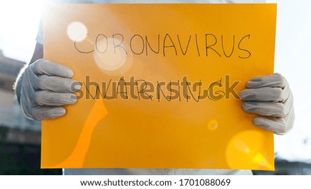 Person with surgical gloves holding yellow sign with coronavirus warning, Covid-19 pandemic.