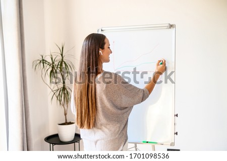 Business, education and office concept. Young woman with flip board in office space writes something, paints some graphic
