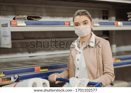 woman with medical facemask standing in market near empty shelves.