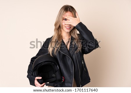 Russian girl with a motorcycle helmet isolated on beige background covering eyes by hands and smiling